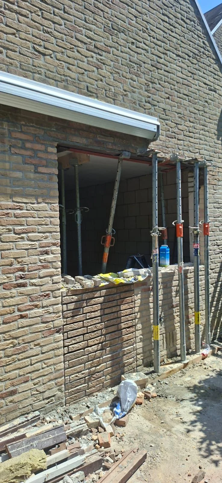 Limburg: buitenzijde van een gemetselde gevel met een opening en tijdelijke ondersteuning.